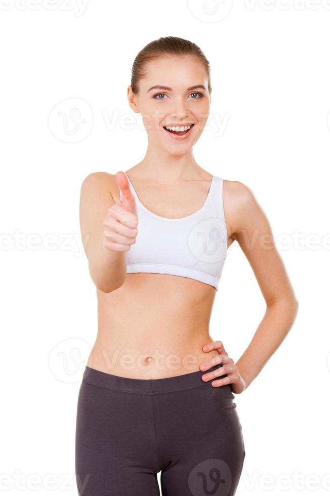 femme sportive. belle jeune femme en vêtements de sport montrant son pouce vers le haut et souriant debout isolé sur blanc photo