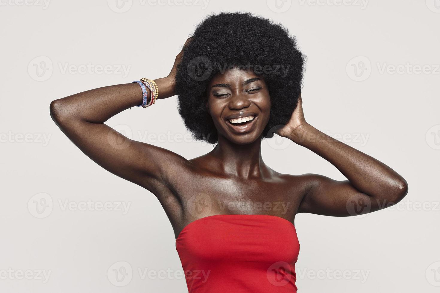 belle jeune femme africaine tenant les mains derrière la tête et souriant en se tenant debout sur fond gris photo