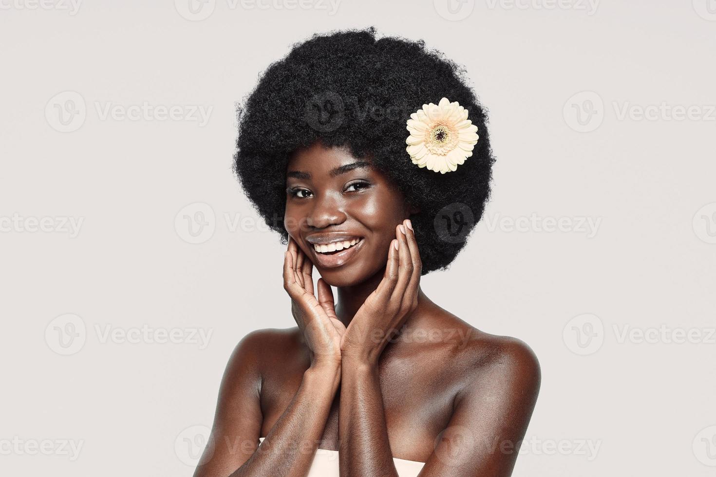 portrait de la belle jeune femme africaine touchant le visage et souriant debout sur fond gris photo
