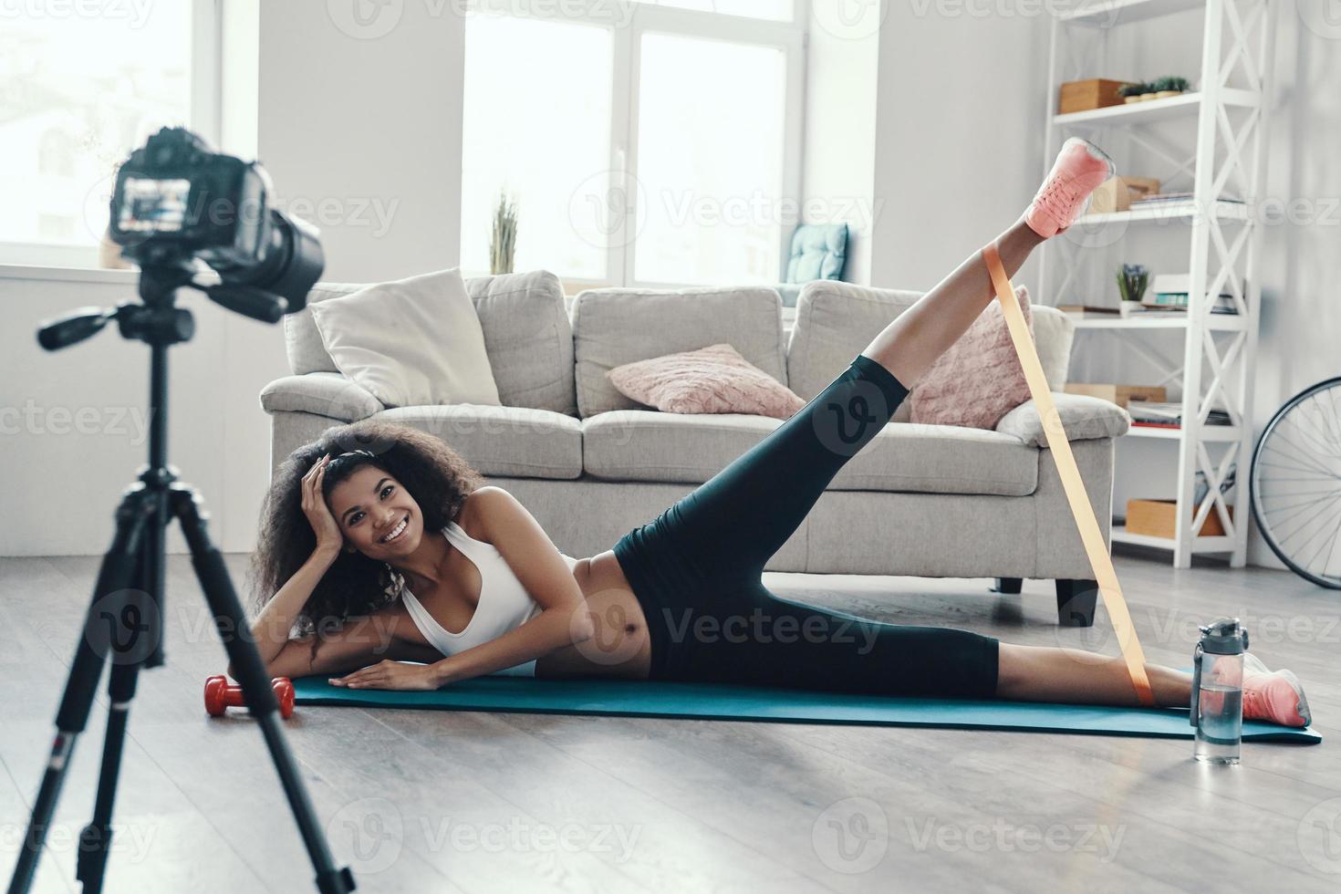 heureuse jeune femme africaine faisant de l'exercice à l'aide d'une sangle et souriant tout en faisant une vidéo sur les réseaux sociaux photo