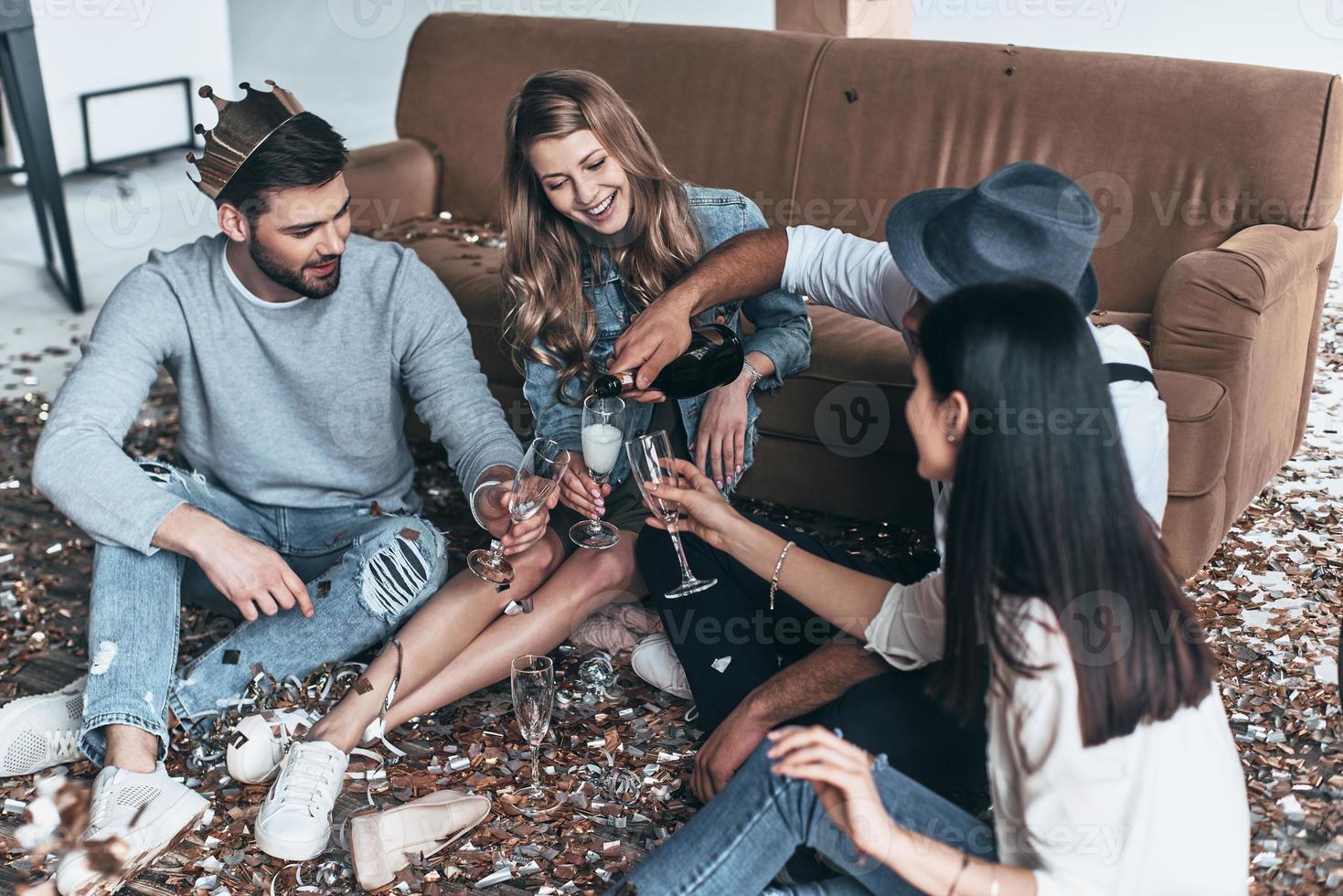 super fête. vue de dessus de jeunes gens modernes versant du champagne assis sur le sol avec des confettis autour photo