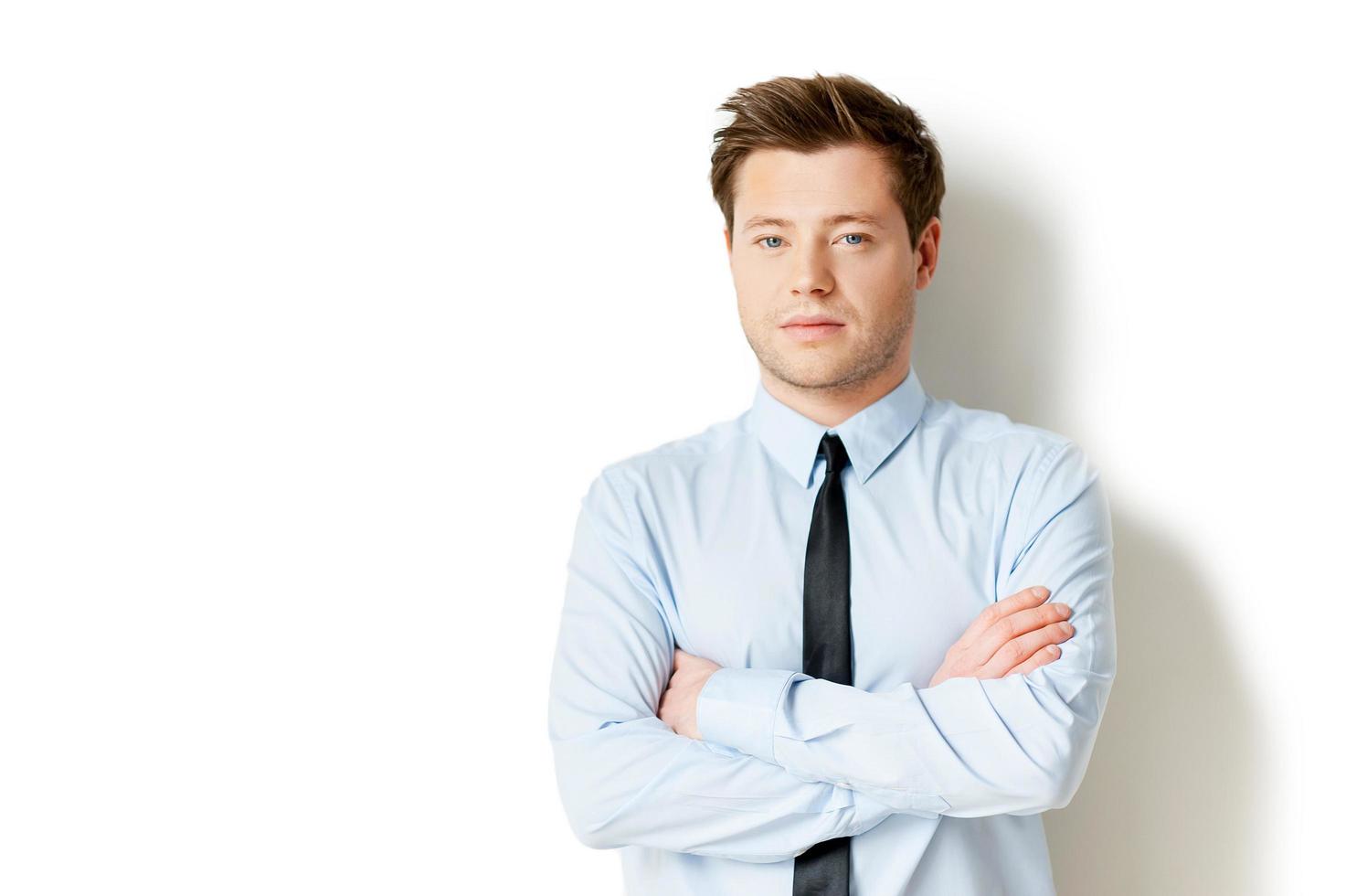 portrait de réussite. beau jeune homme en tenues de soirée regardant la caméra et en gardant les bras croisés en se tenant debout isolé sur blanc photo