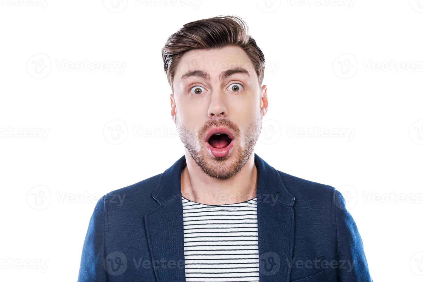 nouvelle choquante. portrait d'un jeune homme choqué regardant la caméra et gardant la bouche ouverte en se tenant debout sur fond blanc photo