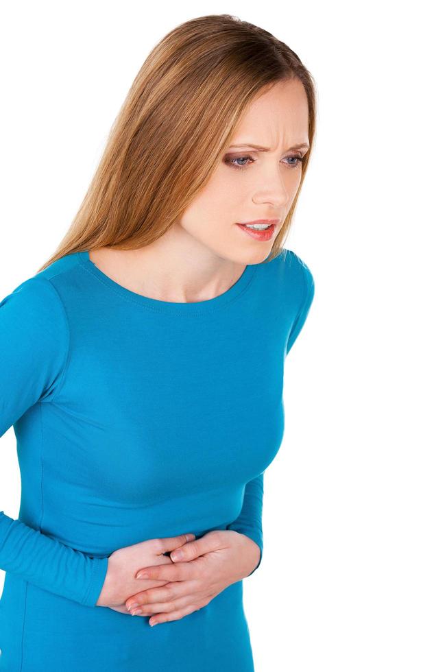 indigestion. jeune femme frustrée tenant les mains sur le ventre et regardant loin en se tenant debout isolé sur blanc photo