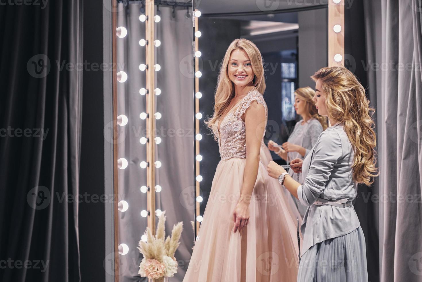 magnifique mariée. jeune femme concentrée mesurant la mariée en se tenant debout dans la cabine d'essayage photo