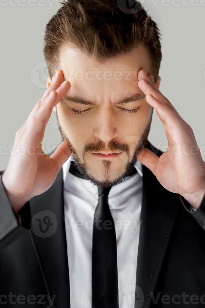 sensation de mal de tête. portrait de jeune homme en tenues de soirée tenant la tête dans les mains et en gardant les yeux fermés en se tenant debout sur fond gris photo