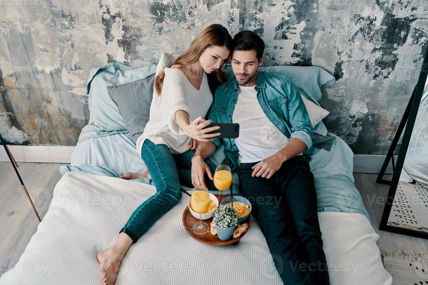 laissez-moi prendre un selfie vue de dessus d'un beau jeune couple prenant un selfie et souriant tout en passant du temps au lit à la maison photo