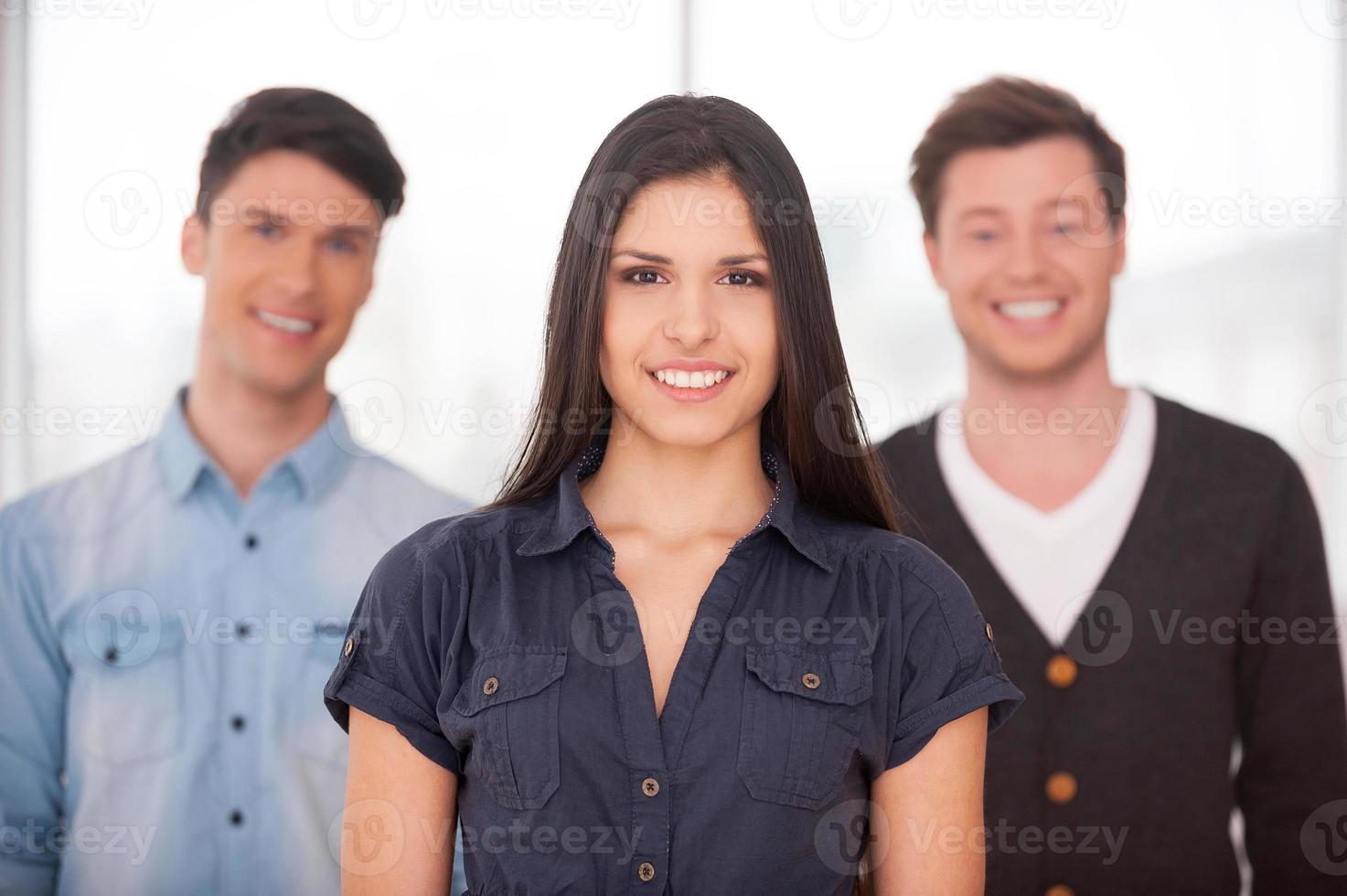 véritable chef. jolie jeune femme souriante tandis que deux hommes debout derrière elle photo