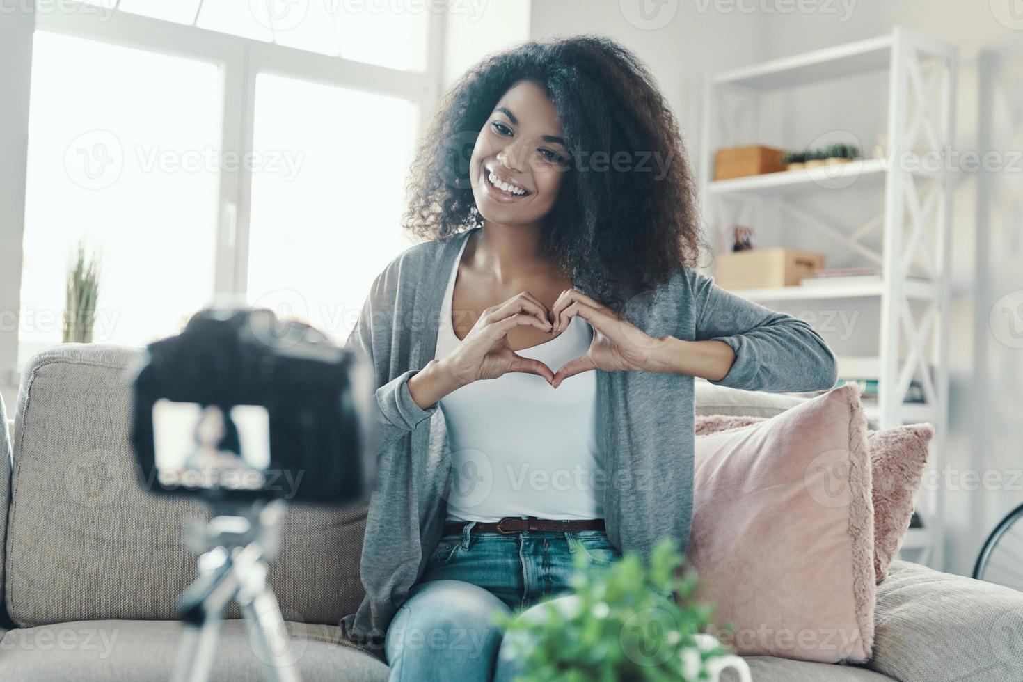 jolie jeune femme africaine montrant le cœur avec ses mains et souriant tout en faisant une vidéo sur les réseaux sociaux photo