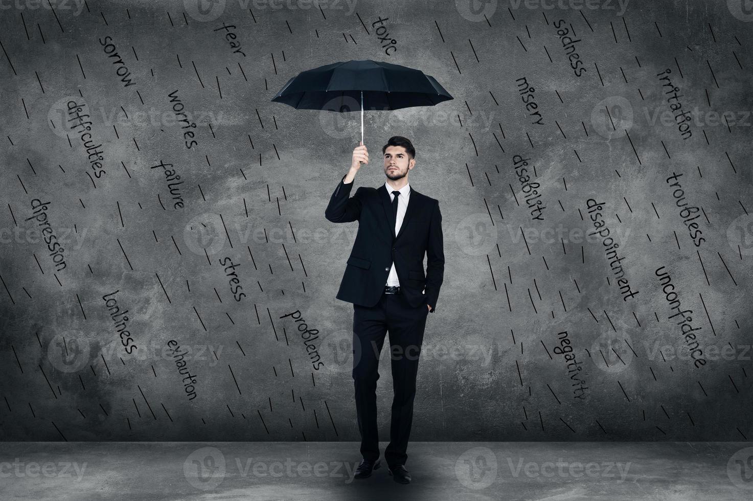 se sentir protégé. toute la longueur d'un jeune homme confiant en costume complet tenant des parapluies tout en se tenant devant le mur de béton photo