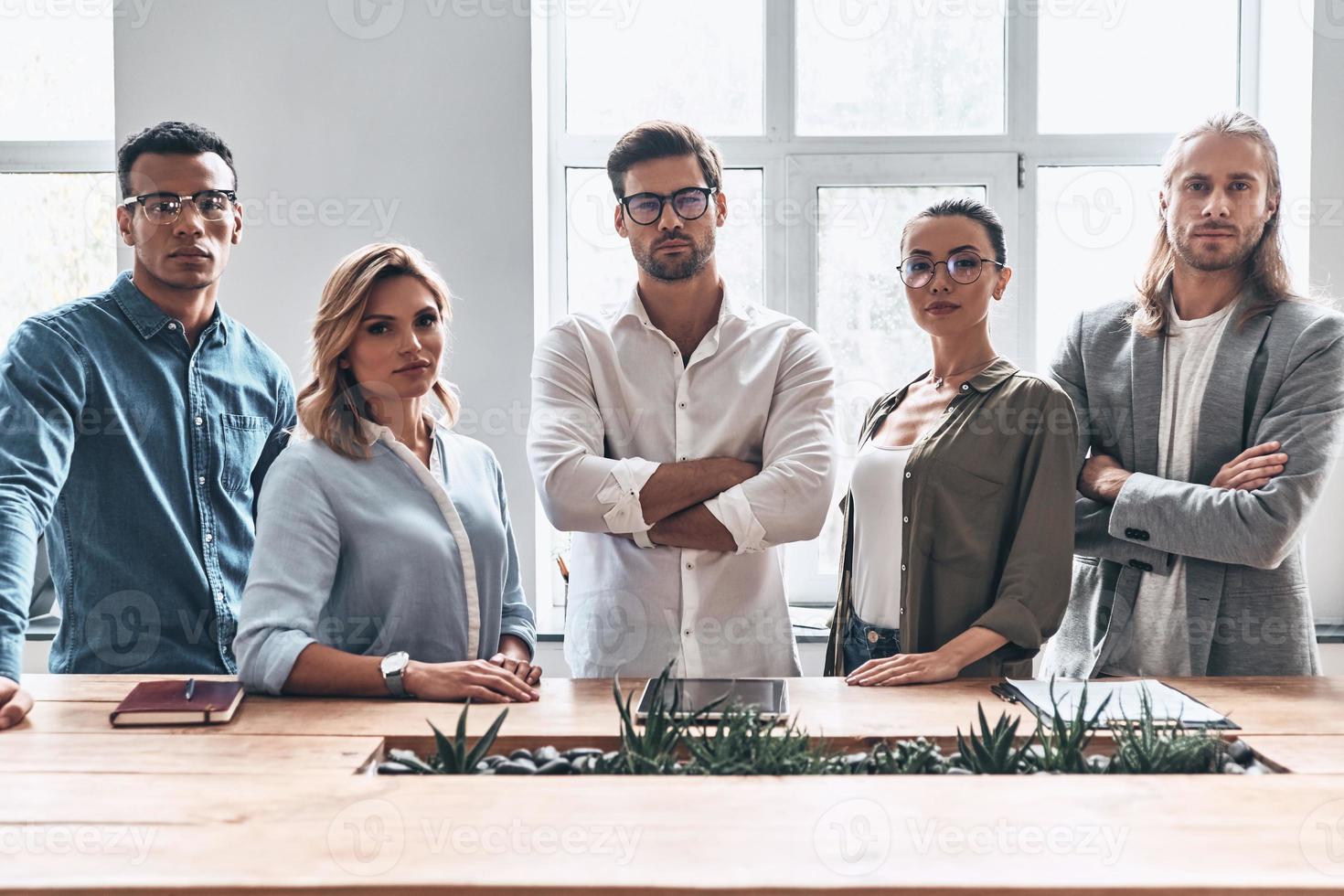 confiant et intelligent. groupe de jeunes gens modernes en vêtements décontractés intelligents regardant la caméra tout en se tenant dans le bureau de création photo