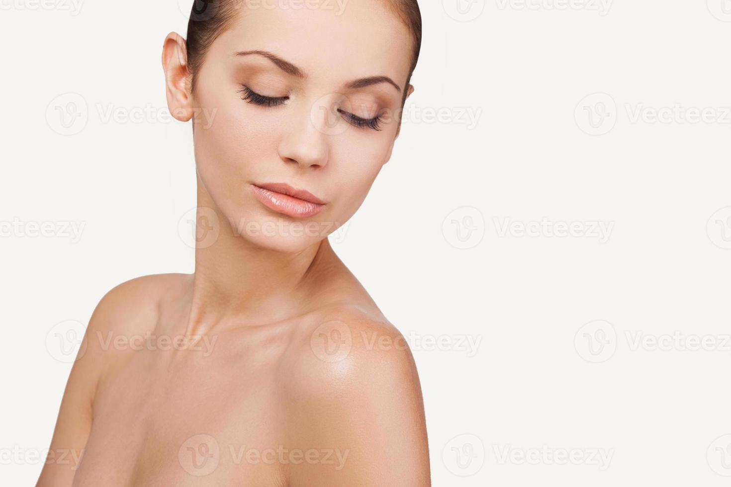 frais et beau. portrait d'une belle jeune femme torse nu gardant les yeux fermés en se tenant debout sur fond gris photo