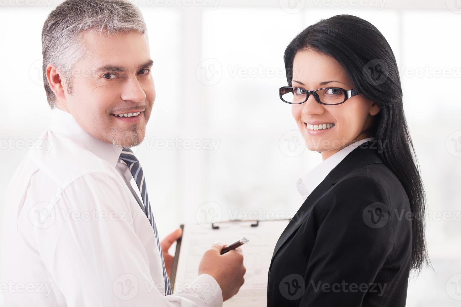 gens d'affaires faisant de la paperasse. deux hommes d'affaires souriants écrivant quelque chose dans un bloc-notes et regardant par-dessus l'épaule photo