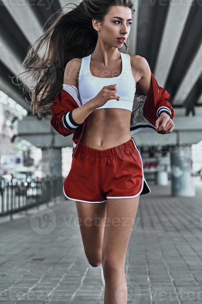 jogging à l'air frais. belle jeune femme en vêtements de sport regardant loin tout en courant sous le pont à l'extérieur photo