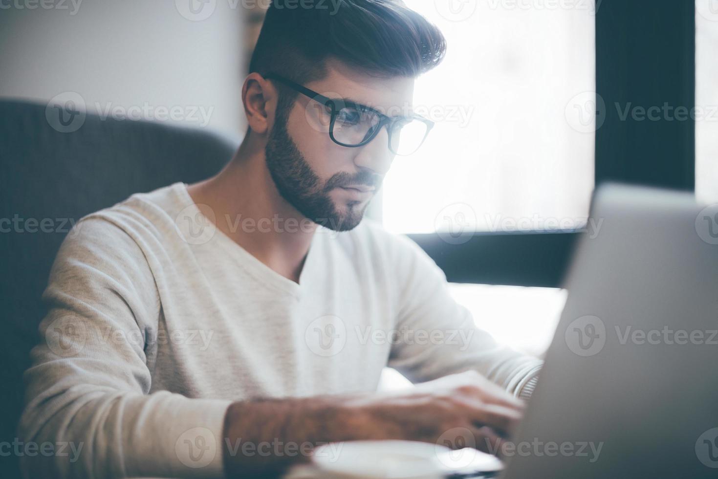 homme d'affaires confiant au travail. jeune homme confiant à lunettes travaillant sur un ordinateur portable assis au bureau ou au café photo