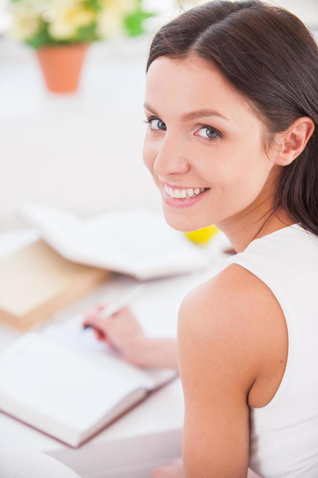 prendre des notes. vue arrière de la belle jeune femme écrivant quelque chose dans son bloc-notes et souriant à la caméra photo