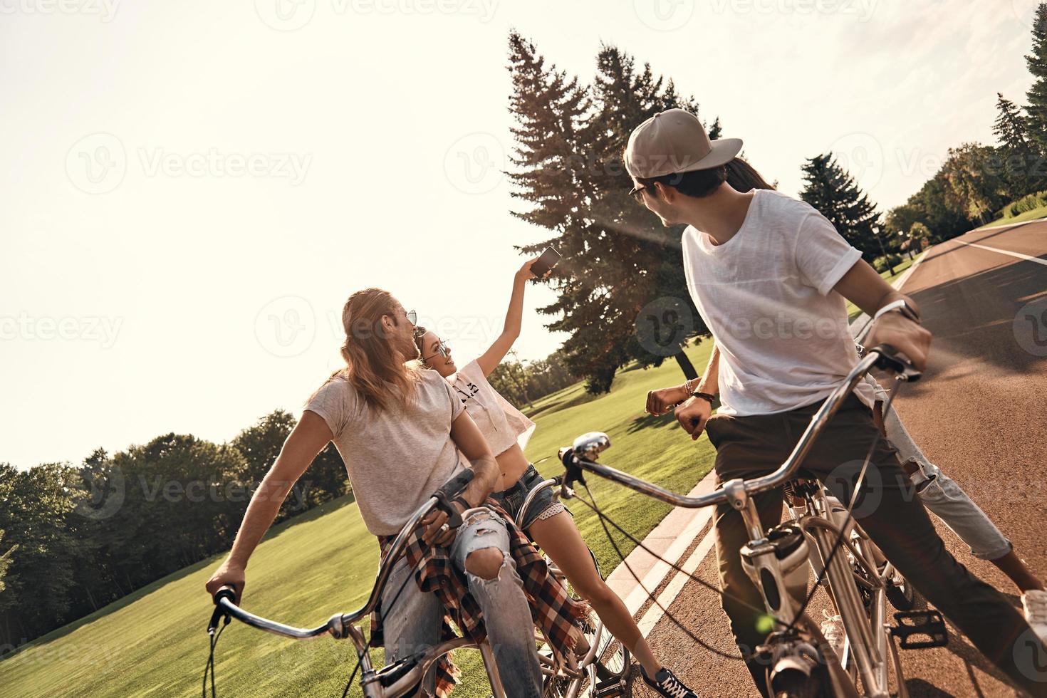 saisir l'instant. groupe de jeunes gens heureux en tenue décontractée prenant selfie et souriant tout en faisant du vélo ensemble à l'extérieur photo