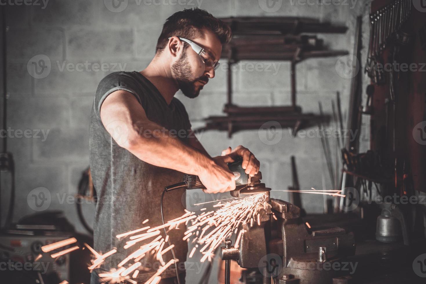 travailleur confiant. jeune homme confiant meulant avec des étincelles dans un atelier de réparation photo