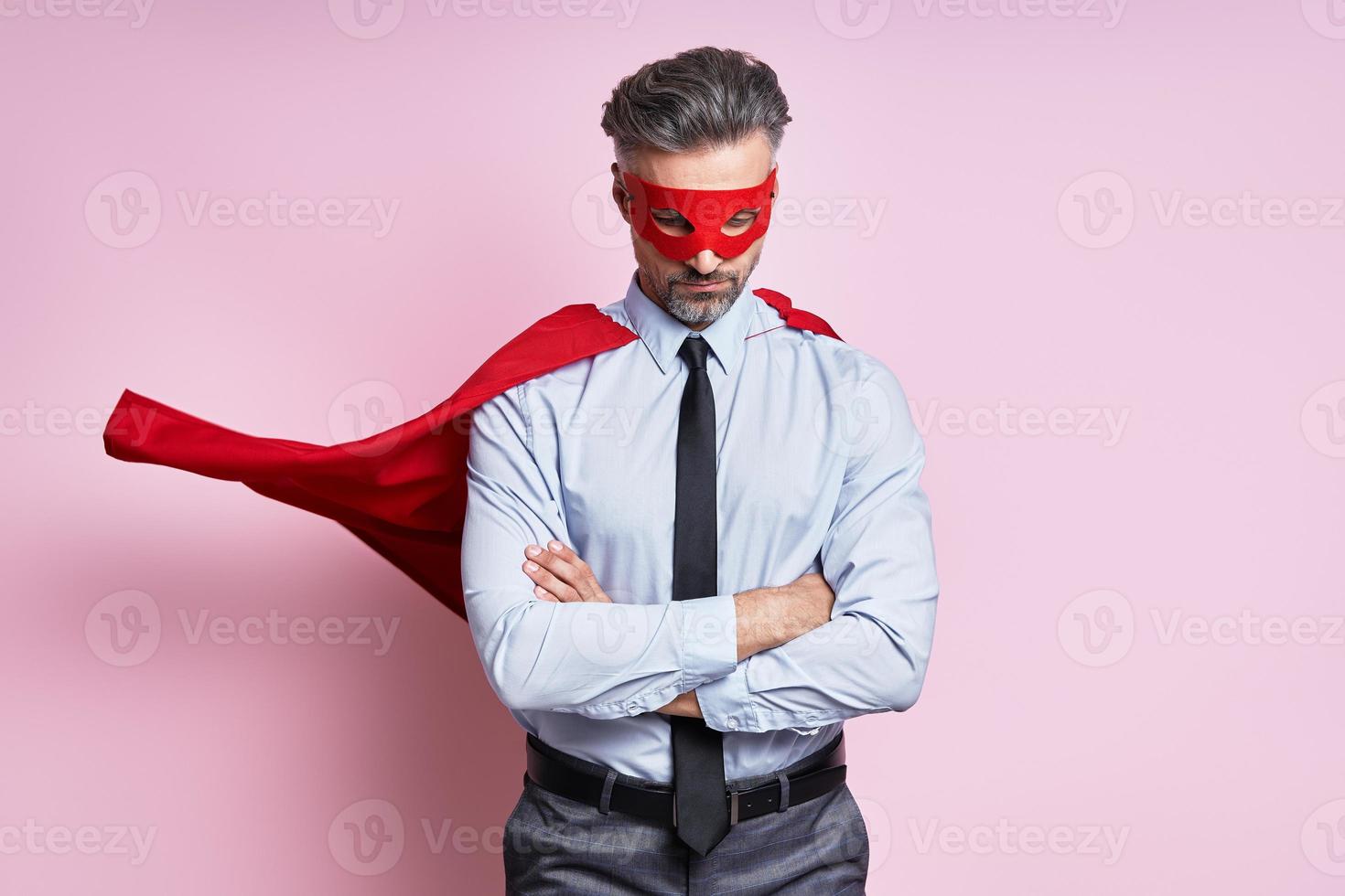 homme mûr confiant en chemise et cravate portant une cape de super-héros en se tenant debout sur fond rose photo
