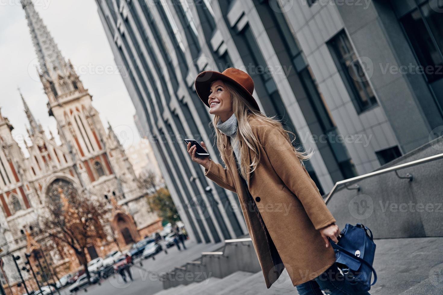 arrêtez-vous et profitez du moment. jolie jeune femme regardant loin et souriant tout en passant du temps sans soucis dans la ville photo