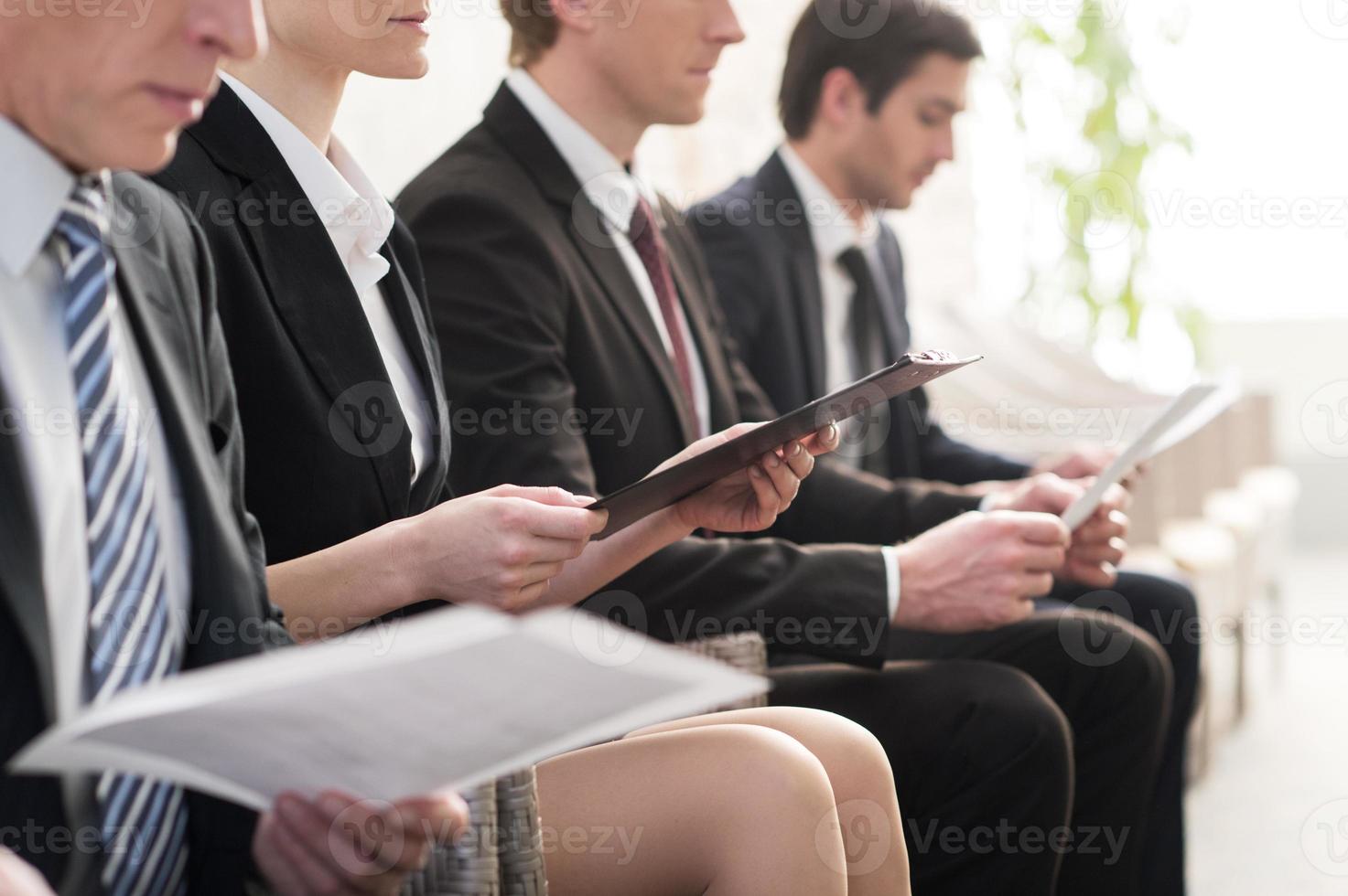 attendre en ligne. image recadrée de personnes en tenues de soirée faisant la queue tout en étant assises sur les chaises et tenant des papiers dans leurs mains photo