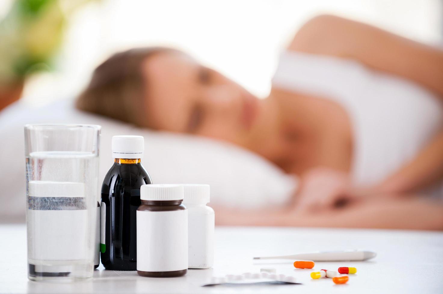 femme malade. jeune femme allongée dans son lit pendant que des médicaments sont posés au premier plan photo