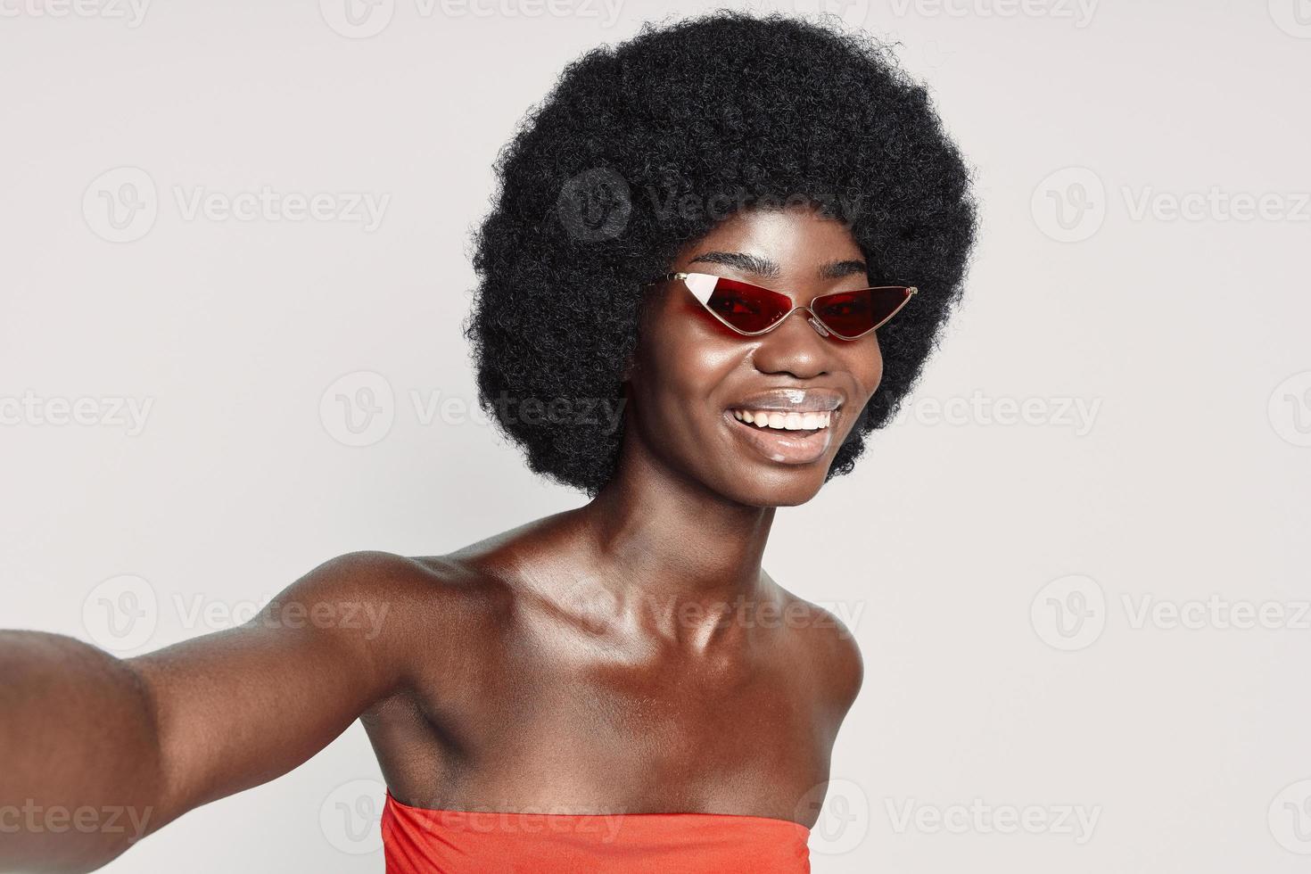 belle jeune femme africaine faisant selfie et souriant debout sur fond gris photo