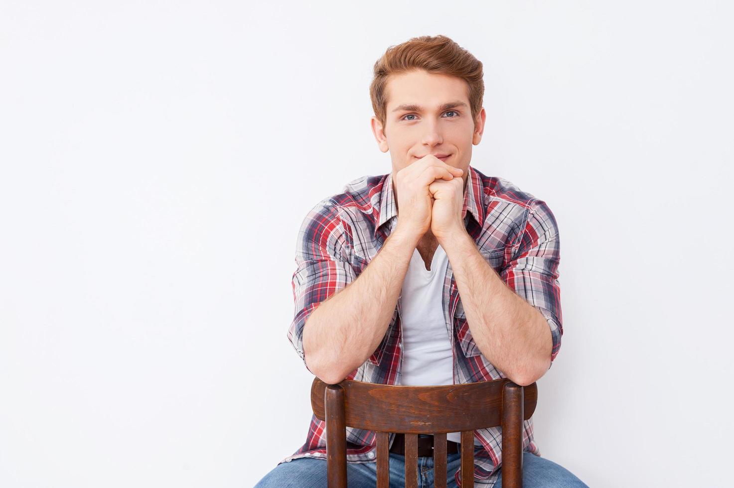 confiant beau. beau jeune homme regardant la caméra assis sur la chaise et sur fond blanc photo