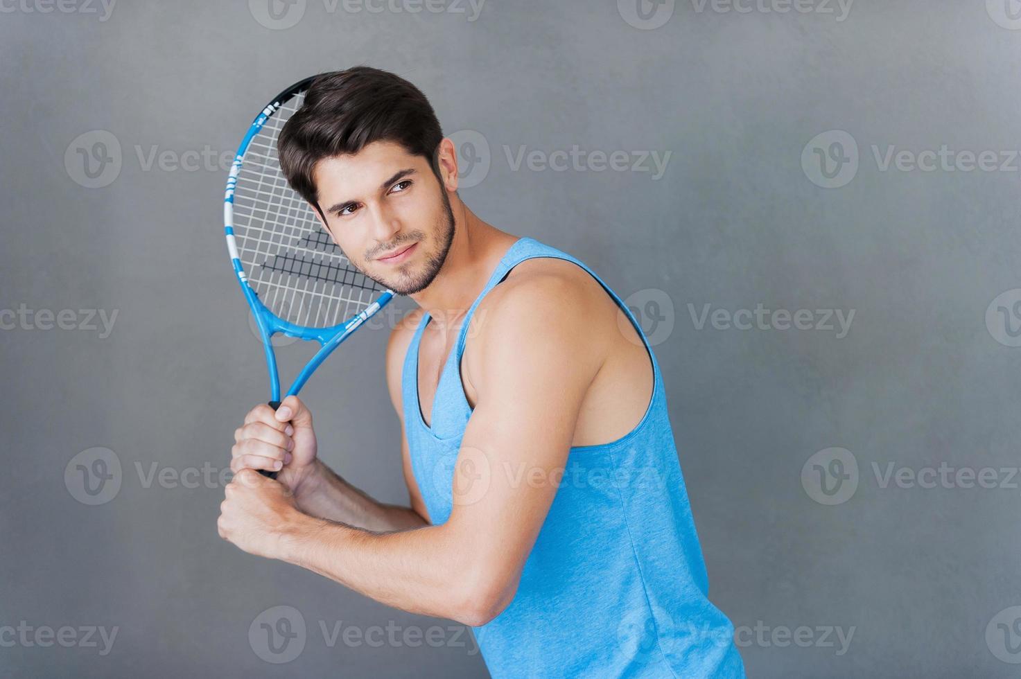 joueur de tennis. confiant jeune homme musclé tenant une raquette de tennis en se tenant debout sur fond gris photo