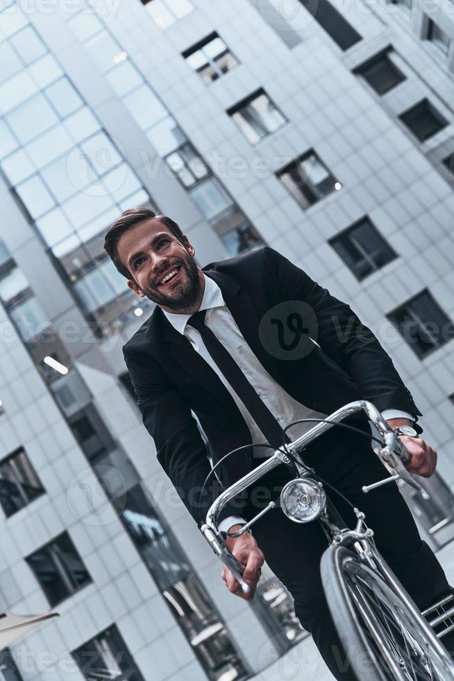 pas de trafic. beau jeune homme en costume complet souriant et impatient tout en faisant du vélo à l'extérieur photo