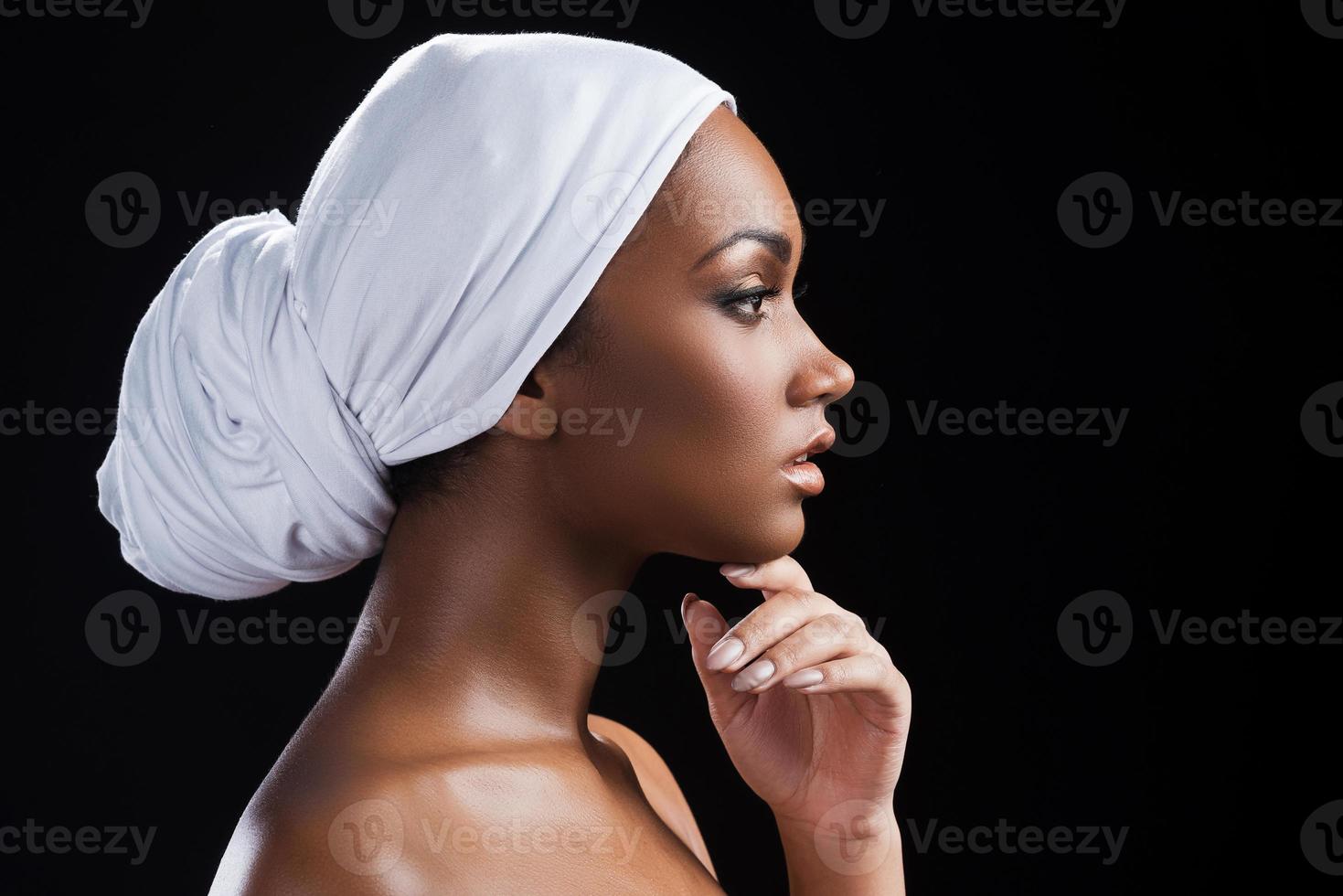 portrait de beauté. vue latérale d'une belle femme africaine portant un foulard et tenant la main sur le menton en se tenant debout sur fond noir photo