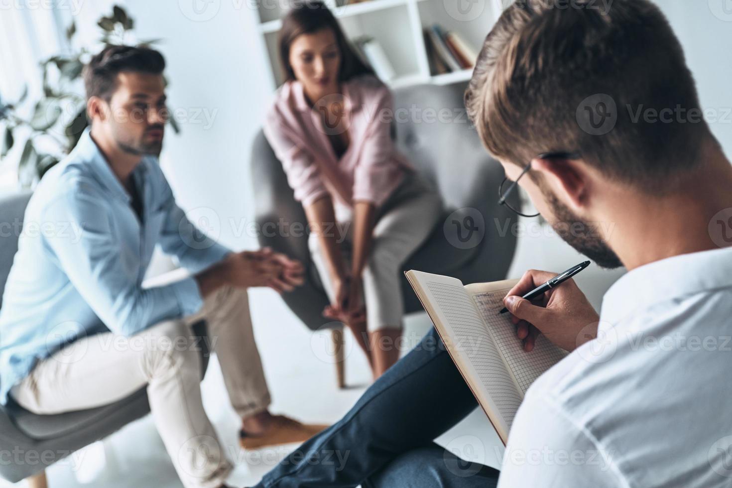 prendre des notes. jeune couple marié parlant assis sur la séance de thérapie avec un psychologue photo