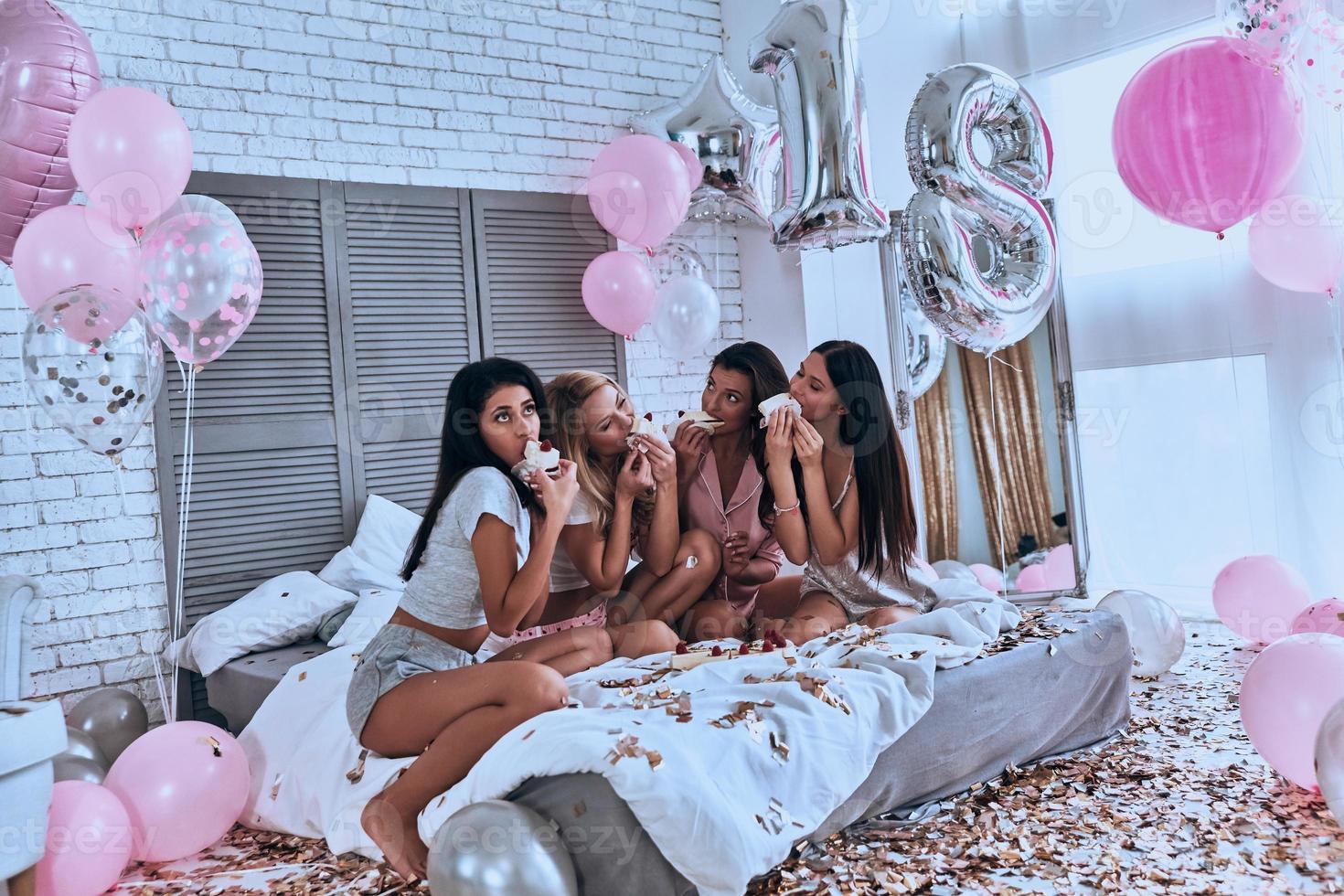 alors goûtez quatre belles jeunes femmes en pyjama mangeant du gâteau tout en organisant une soirée pyjama dans la chambre avec des ballons partout photo