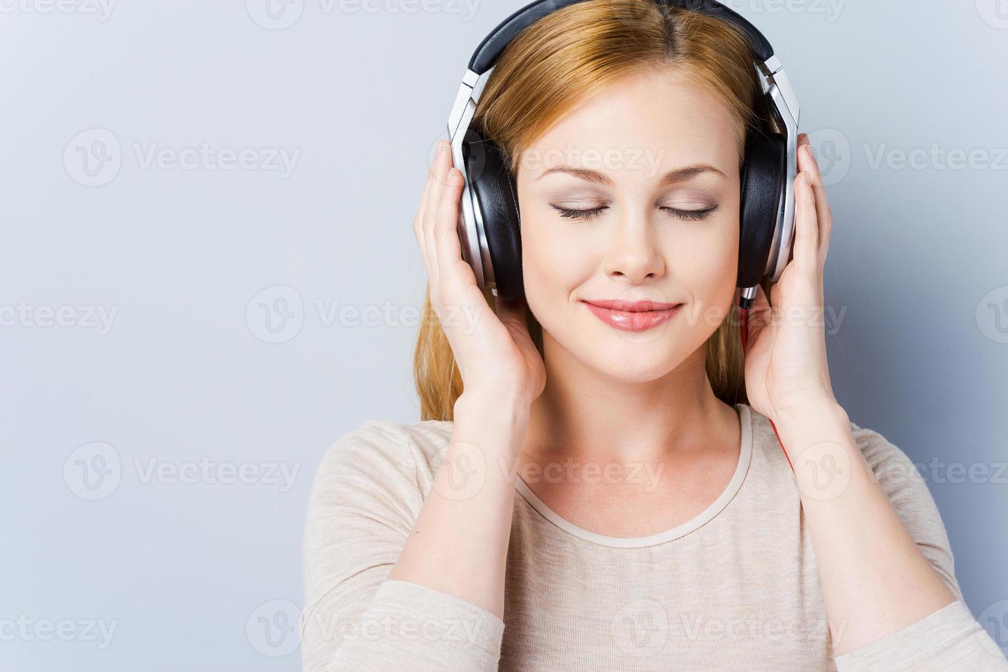 ondes musicales. belles jeunes femmes dans les écouteurs en gardant les yeux fermés et souriant tout en se tenant sur fond gris photo