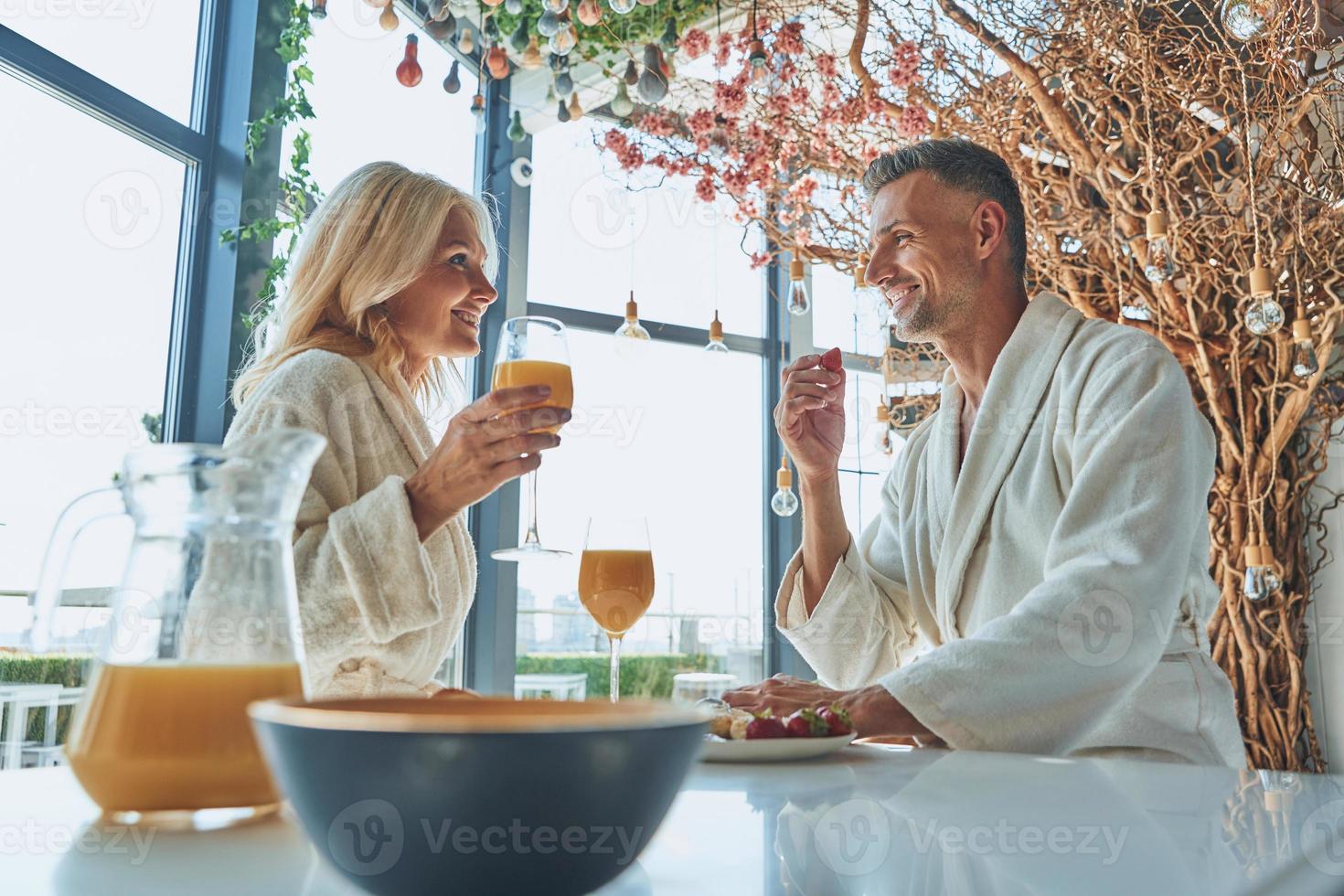 beau couple mature en peignoirs prenant son petit déjeuner ensemble tout en passant du temps dans la cuisine domestique photo