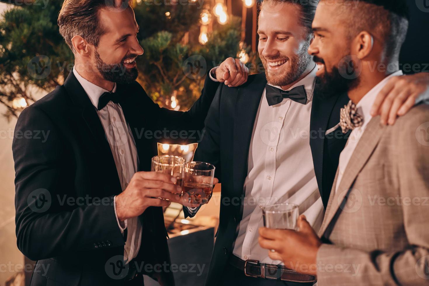 trois hommes en costumes et noeuds papillon buvant du whisky et communiquant tout en passant du temps à la fête photo