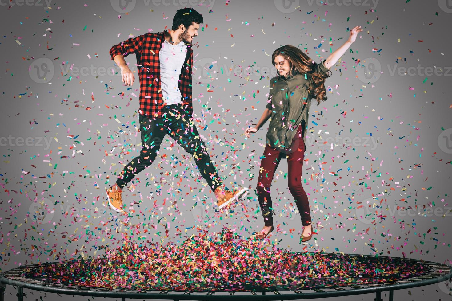 plaisir des confettis. tir en l'air d'un beau jeune couple joyeux sautant sur un trampoline avec des confettis tout autour d'eux photo