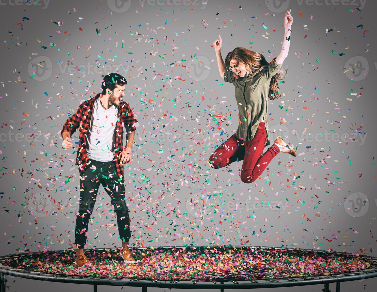 moment de plaisir ensemble. tir en l'air d'un beau jeune couple joyeux sautant sur un trampoline avec des confettis tout autour d'eux photo