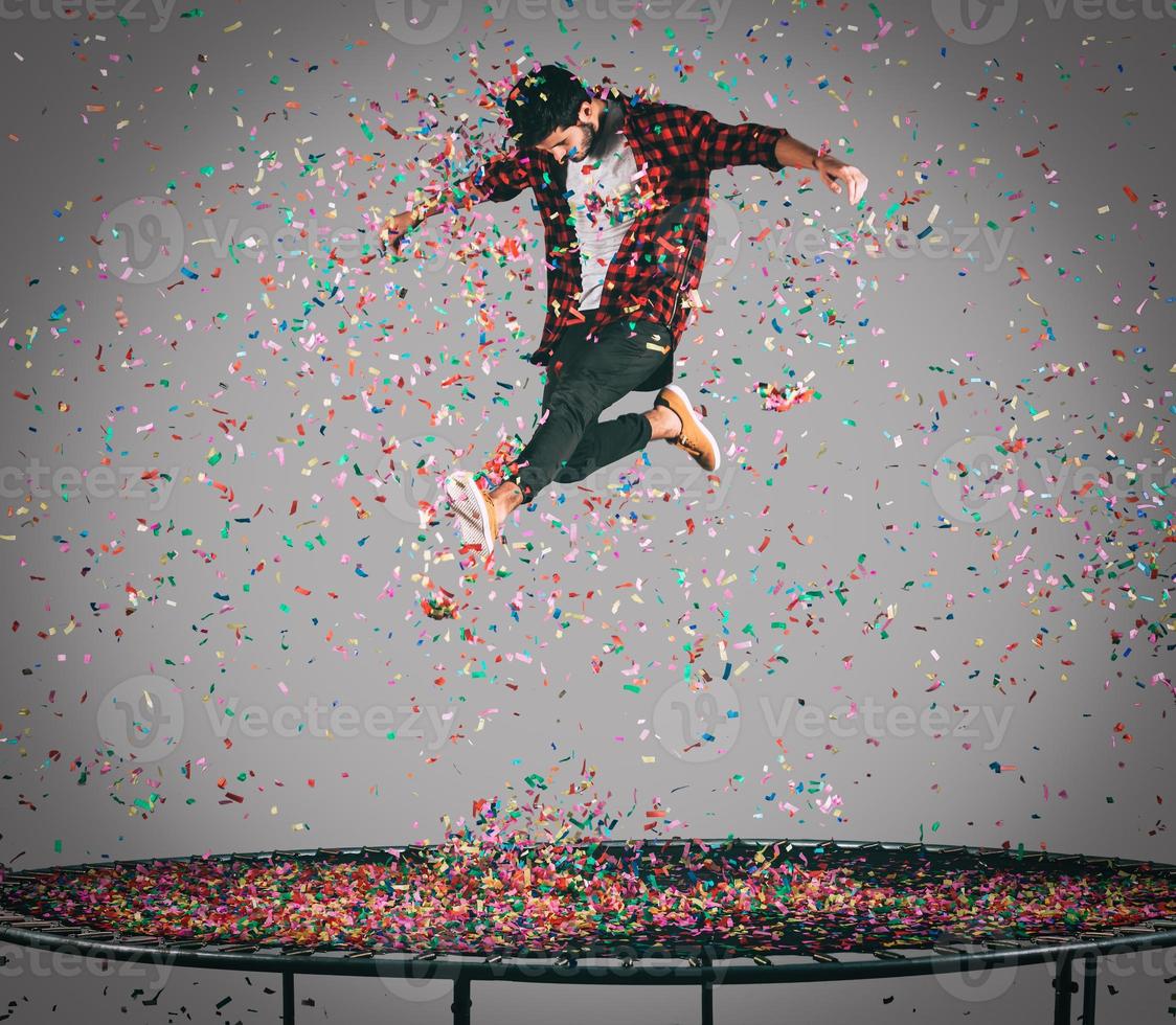 plaisir insouciant. tir en l'air d'un beau jeune homme sautant sur un trampoline avec des confettis tout autour de lui photo