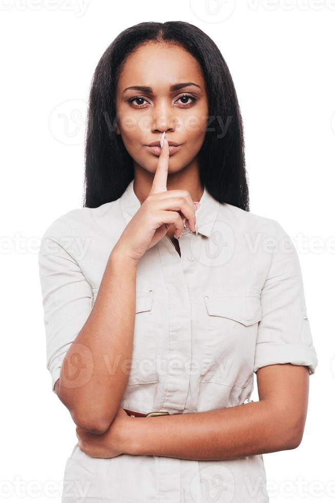 garder le silence confiant jeune femme africaine tenant le doigt sur les lèvres en se tenant debout sur fond blanc photo