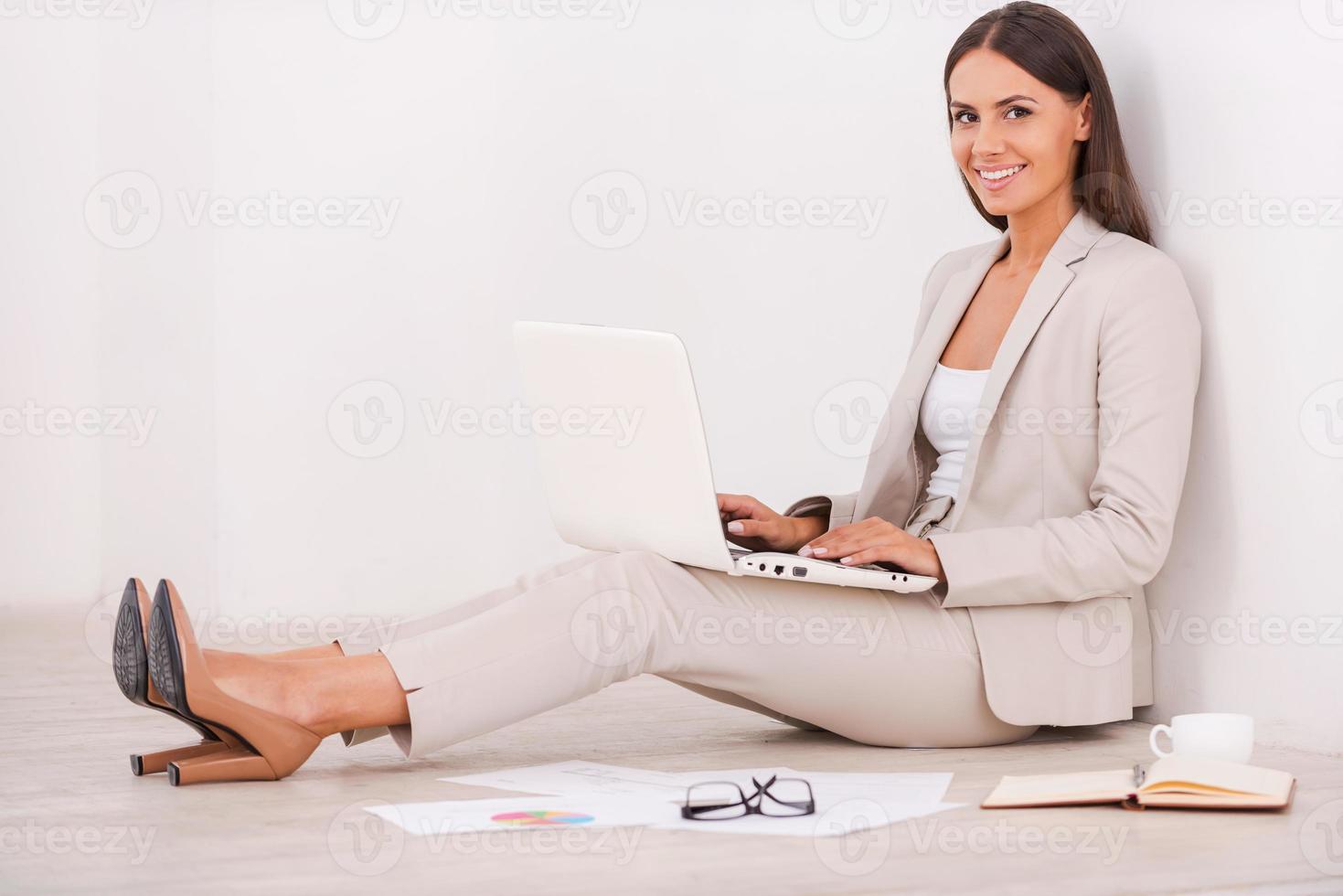 trouver un lieu de travail paisible. vue latérale d'une belle jeune femme d'affaires travaillant sur un ordinateur portable et souriant assis sur le sol photo