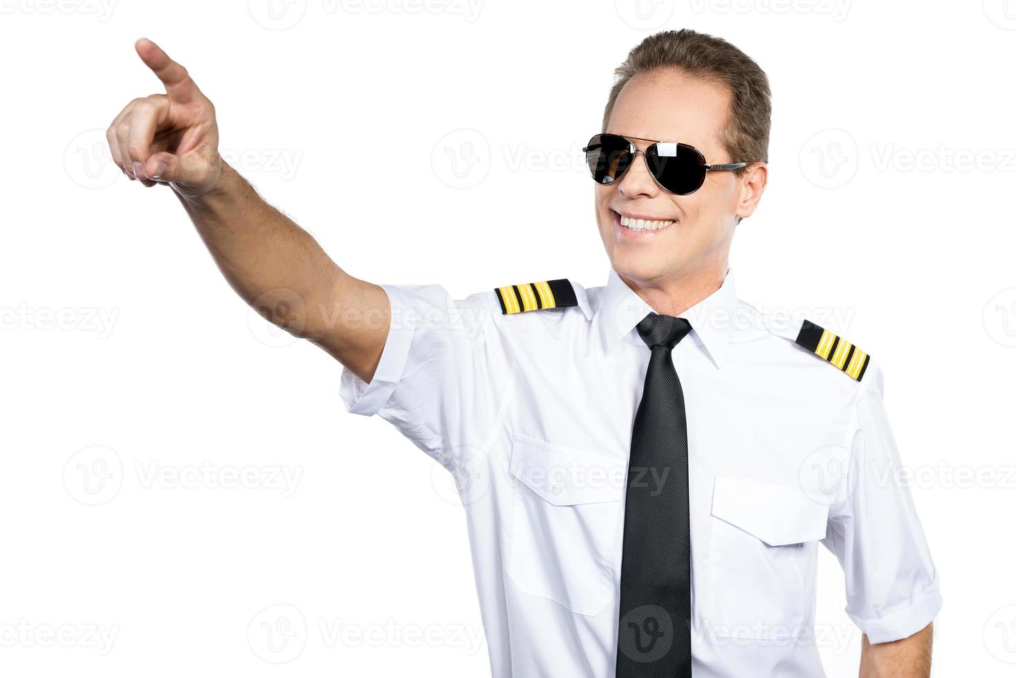 amoureux du ciel. pilote masculin confiant en uniforme pointant vers l'extérieur et souriant en se tenant debout sur fond blanc photo