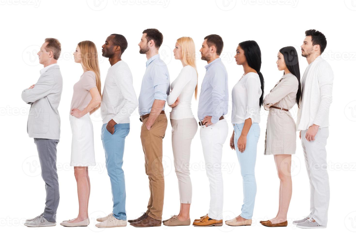 debout dans une rangée. toute la longueur d'un groupe multiethnique confiant de personnes en vêtements décontractés intelligents regardant loin tout en se tenant dans une rangée et sur fond blanc photo