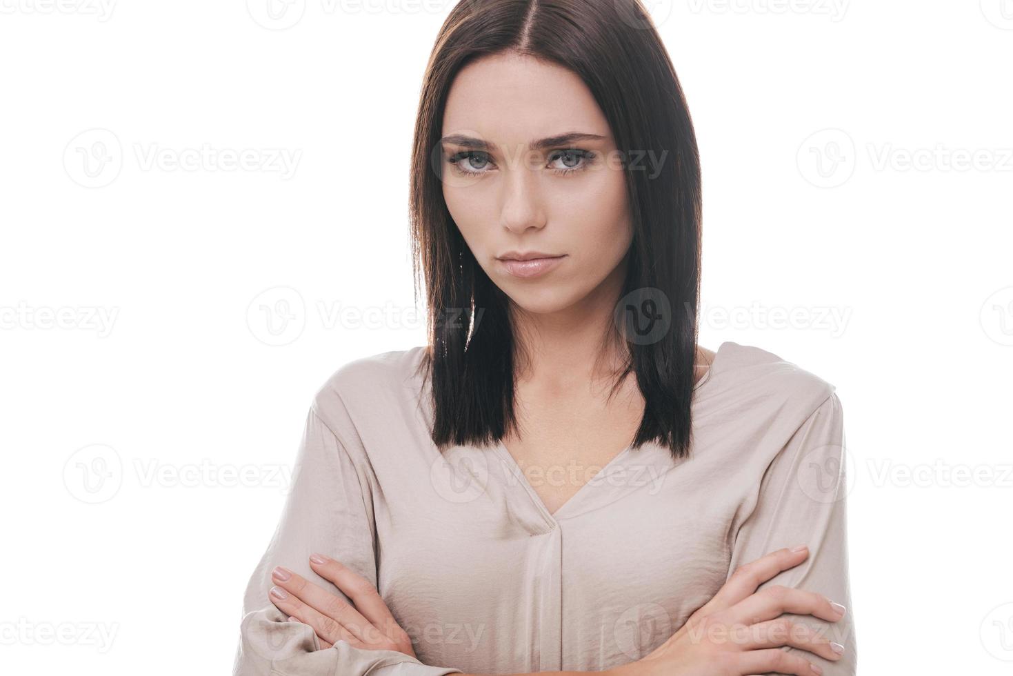 se sentir mécontent. triste jeune femme en tenue décontractée intelligente en gardant les bras croisés et en regardant la caméra en se tenant debout sur fond blanc photo