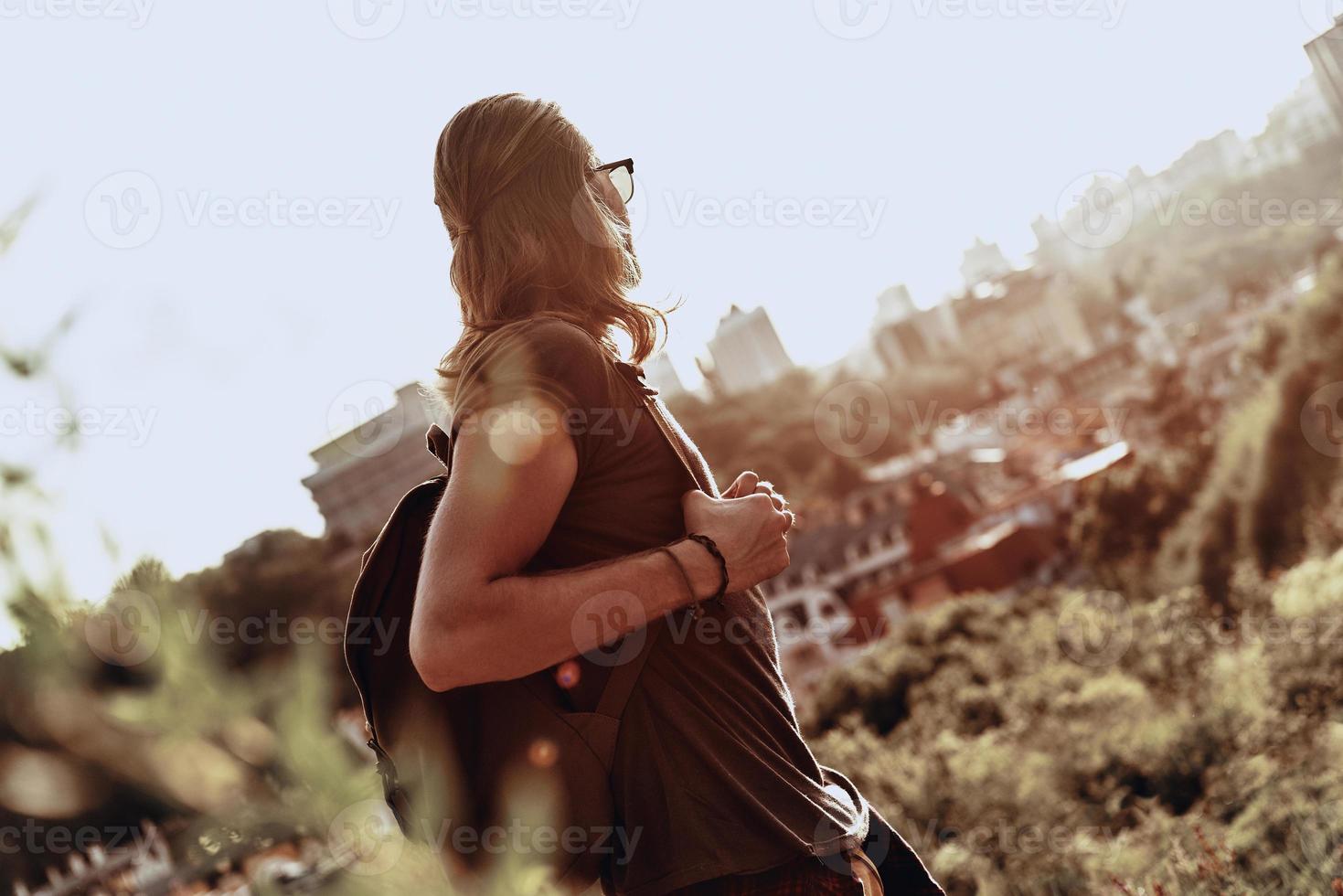 émerveillé par la beauté. jeune homme en vêtements décontractés regardant la vue en se tenant debout sur la colline à l'extérieur photo