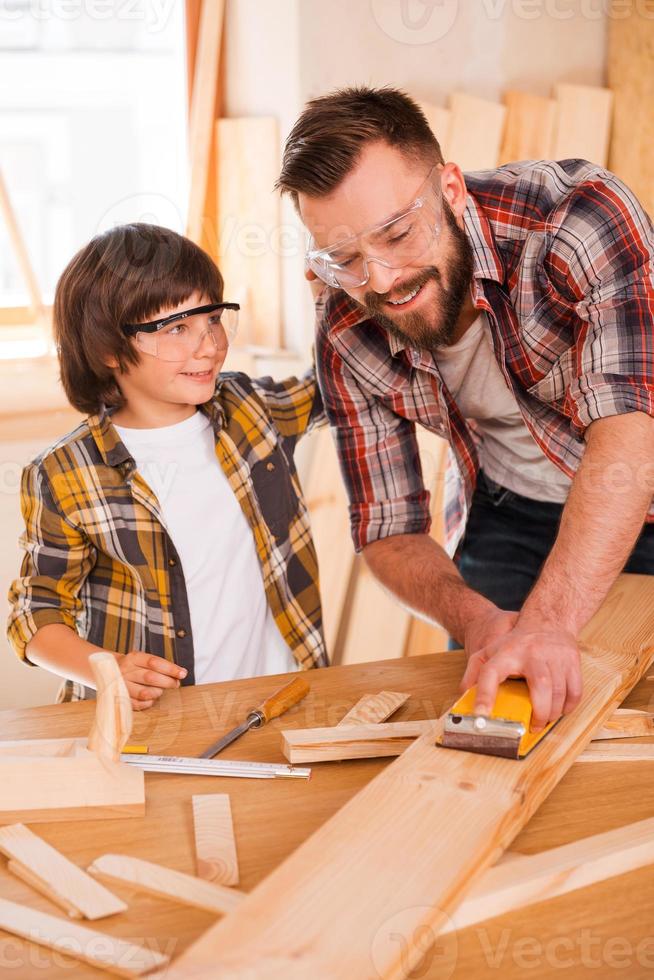 s'amuser en travaillant ensemble. jeune menuisier souriant montrant à son fils comment poncer le bois dans son atelier photo