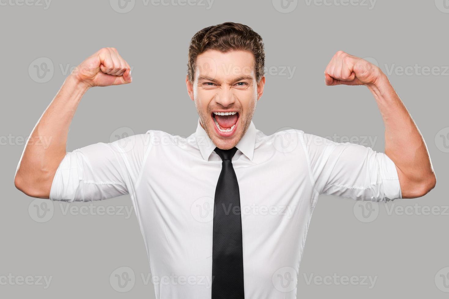 possibilités cachées. beau jeune homme en chemise et cravate regardant la caméra et montrant ses biceps en se tenant debout sur fond gris photo