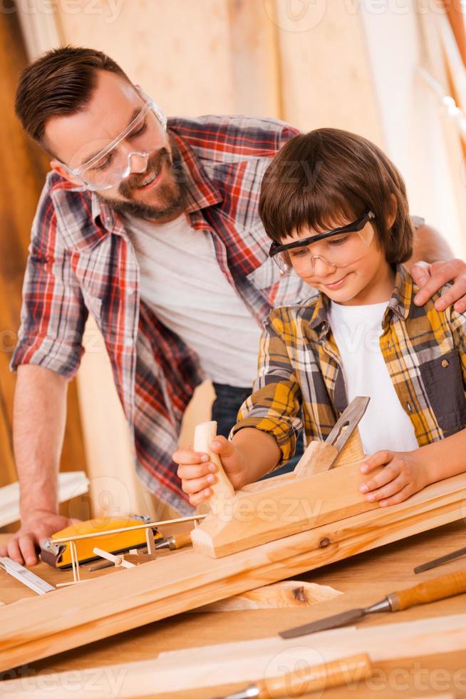 enseigner à son fils tout ce qu'il faut savoir sur la menuiserie. heureux jeune charpentier masculin embrassant son fils tout en travaillant avec du bois dans son atelier photo