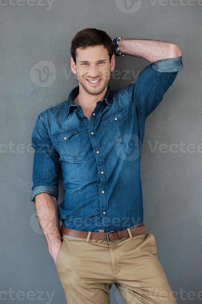 cool et décontracté. souriant jeune homme posant en se tenant debout sur fond gris photo