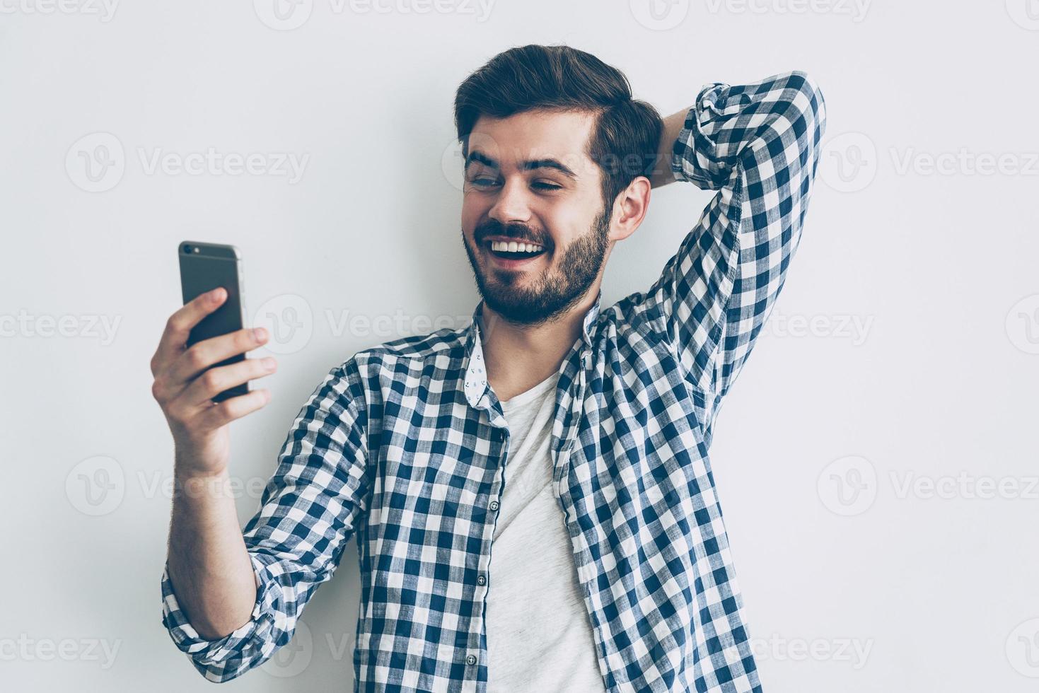 bonne nouvelle d'un ami. heureux jeune homme tenant un téléphone intelligent et le regardant avec le sourire photo